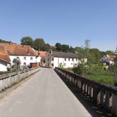 Asphaltierte Brücke mit Betonsteingeländer und Ansicht auf das kleine Dorf