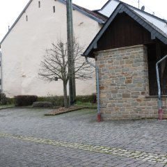 aus hellem Sandstein gemauerte kleine Buswartehalle mit Satteldach