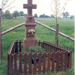 Wegekreuz im Ort mit kleiner Einfriedung eines Gartenzaunes