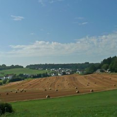 Fernblick auf die Ortsgemeinde Neuheilenbach im Sommer vor einer abgeernteten Strohfeld