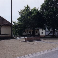 Dorfbrunnen mit Sandsteintrog und geschottertem Parkplatz