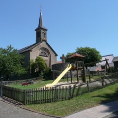 einschiffige Kirche in Sandsteinbauweise - davor Kinderspielplatz