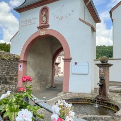 Südtor des Klosters mit Sonnenuhr und Blumen und Brunnen im Vordergrund