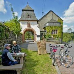Zwei Radfahrer machen Rast auf einer Bank vor der Einfahrt zum Kloster