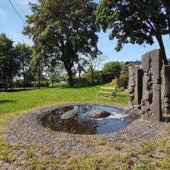 Dreisteliger Steinbrunnen mit rundem Bassin aus Kopfsteinpflaster