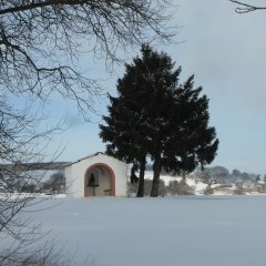 Kleine Kapelle mit offenem Rundbogen in einer Winterlandschaft