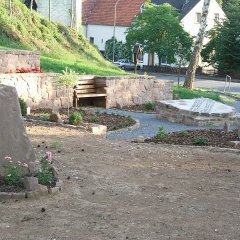 mit Sandsteinen gestalteter Ortseingangsbereich mit großem Wappen und Ruhebank