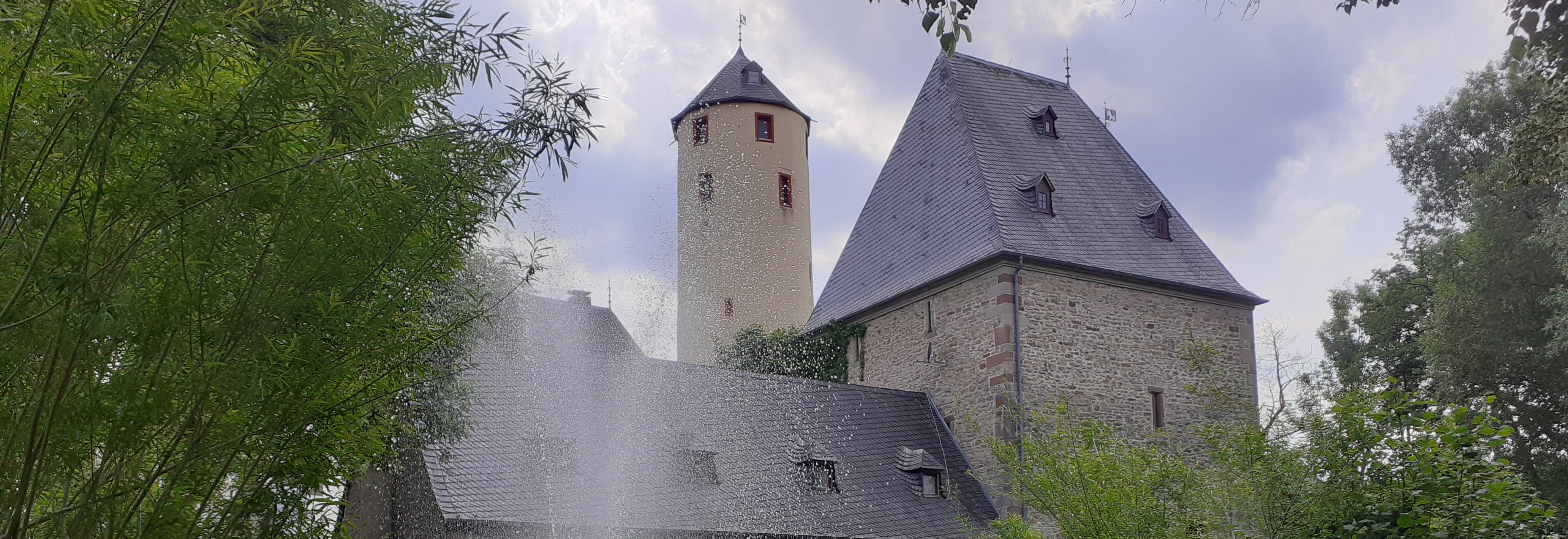 Burganlage mit Burgturm in der Seitenansicht mit Wasserfontäne davor
